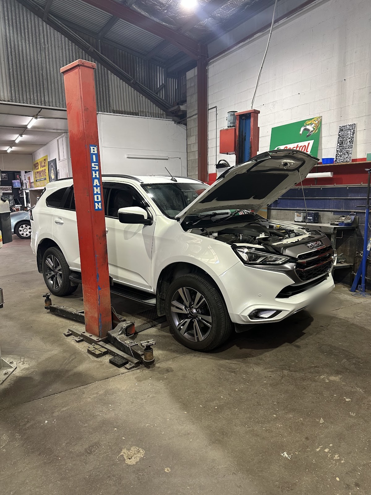 White Isuzu MU-X with the bonnet up beside a Bishamon hoist in the workshop