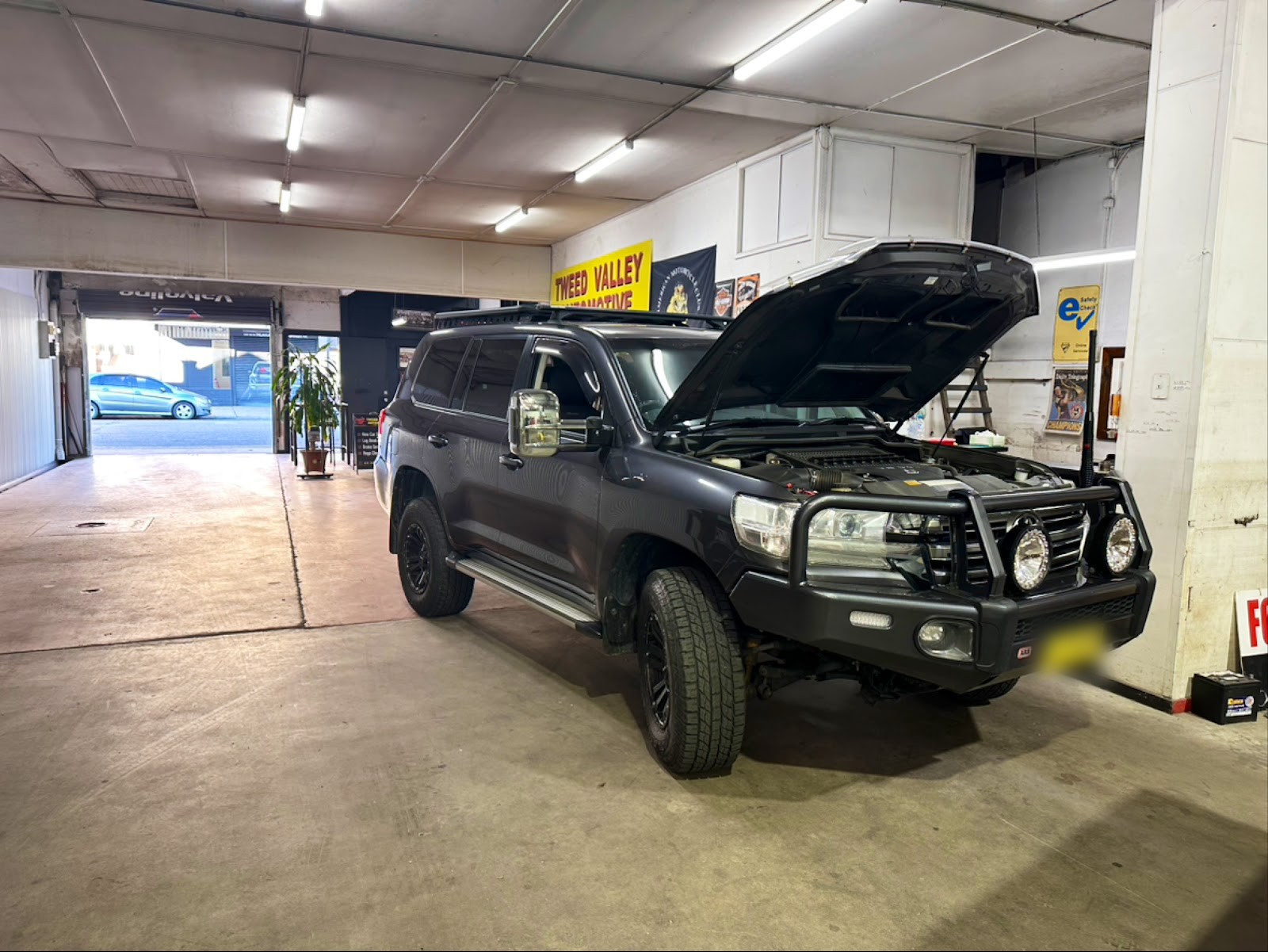 Black Toyota LandCruiser with a bullbar and spotlights, bonnet up inside the workshop