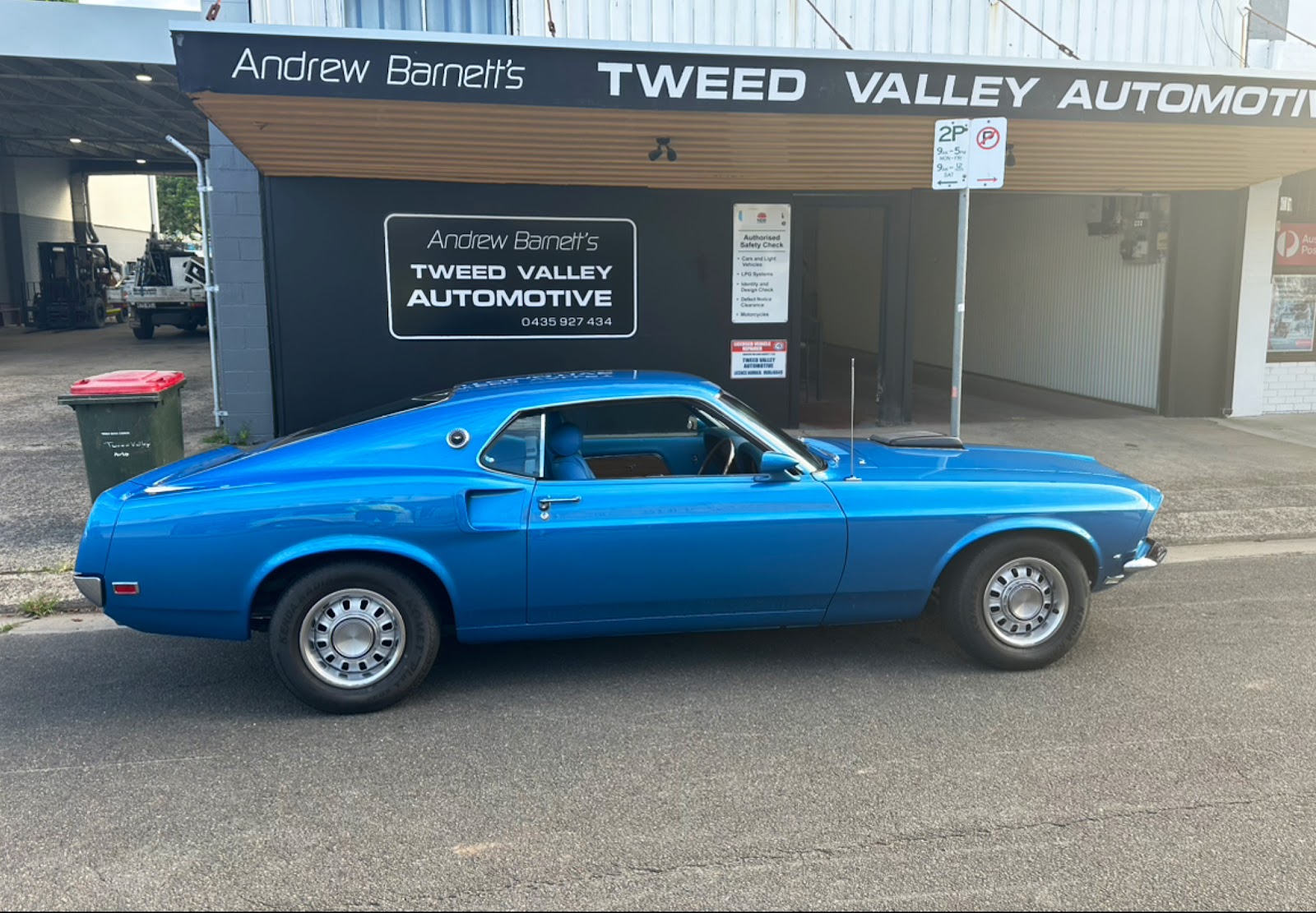 A blue classic Ford Mustang fastback parked outside the Tweed Valley Automotive shopfront on Prospero St