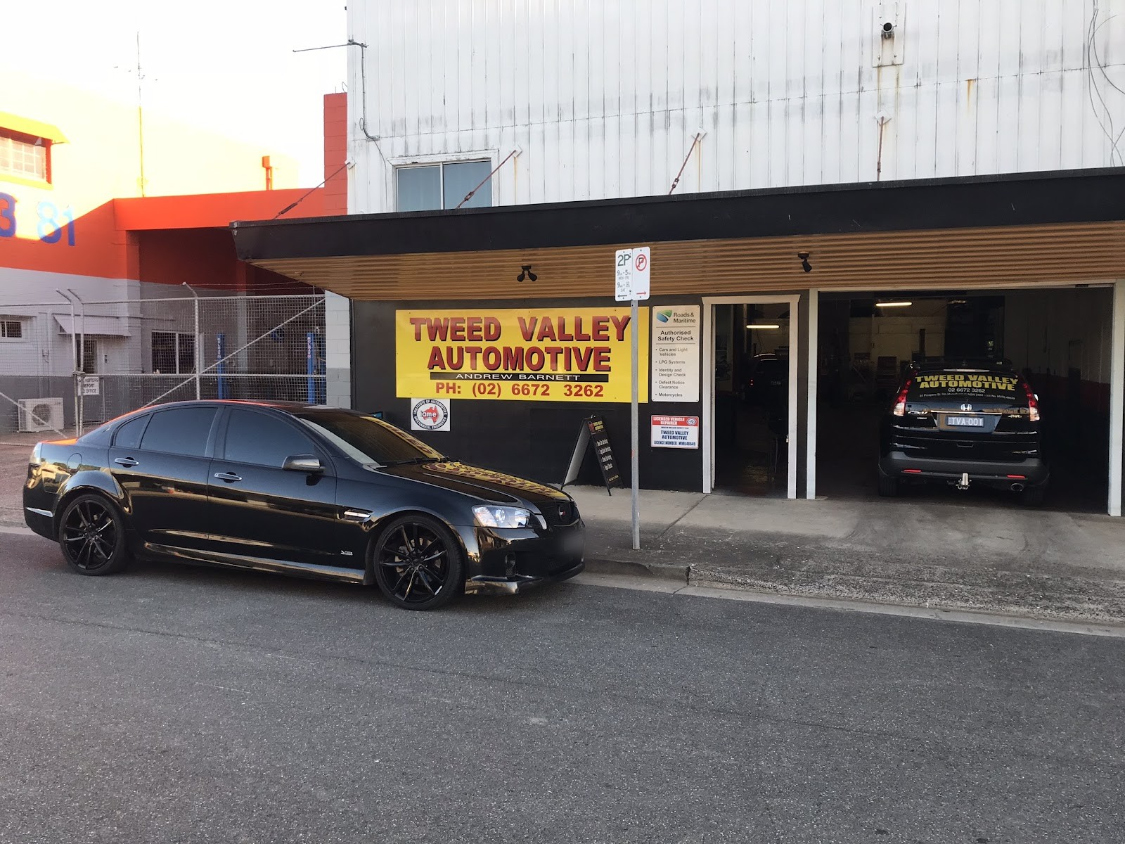 The shopfront under the old yellow Tweed Valley Automotive sign, with a black Commodore out front